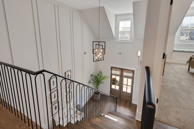 staircase with carpet flooring, visible vents, vaulted ceiling, french doors, and an inviting chandelier