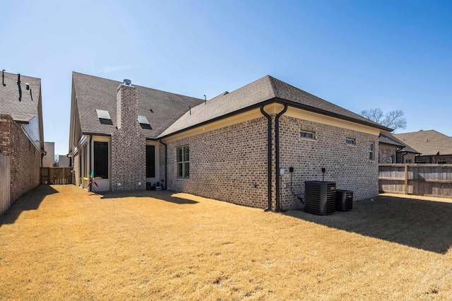 rear view of house featuring central AC, brick siding, a lawn, and a fenced backyard