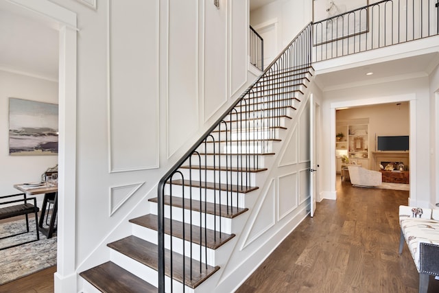 stairs with a high ceiling, crown molding, baseboards, and wood finished floors