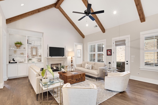 living area featuring a lit fireplace, high vaulted ceiling, beamed ceiling, and wood finished floors