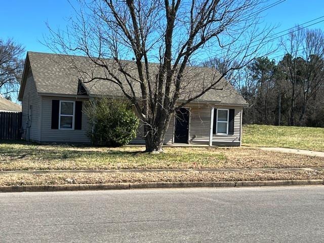 view of front of house with a front lawn, roof with shingles, and fence