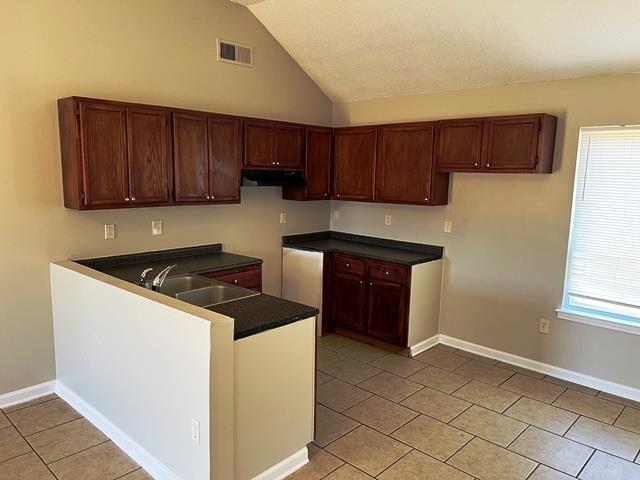 kitchen with dark countertops, a sink, a peninsula, and baseboards