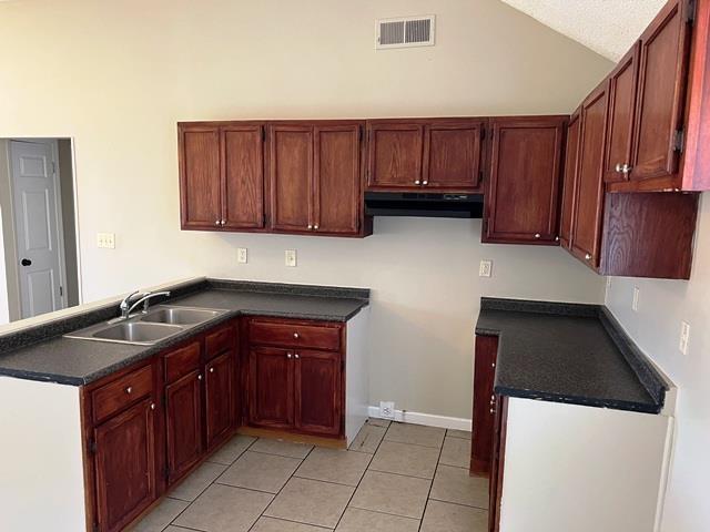 kitchen featuring dark countertops, visible vents, a sink, a peninsula, and under cabinet range hood