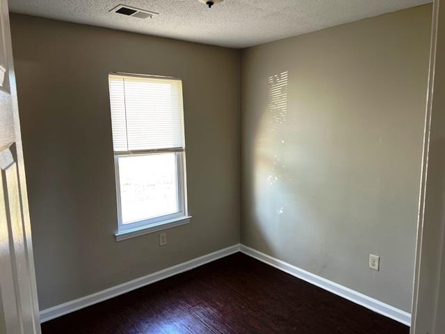 empty room featuring a textured ceiling, dark wood finished floors, visible vents, and baseboards