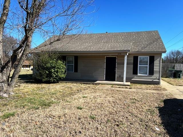 view of front facade featuring roof with shingles, fence, and a front lawn