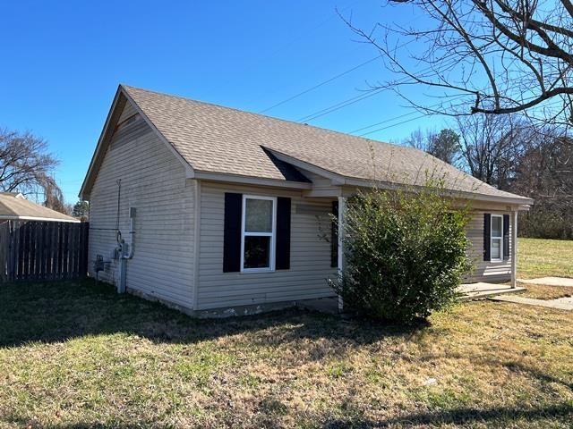 view of home's exterior featuring a shingled roof, fence, and a yard