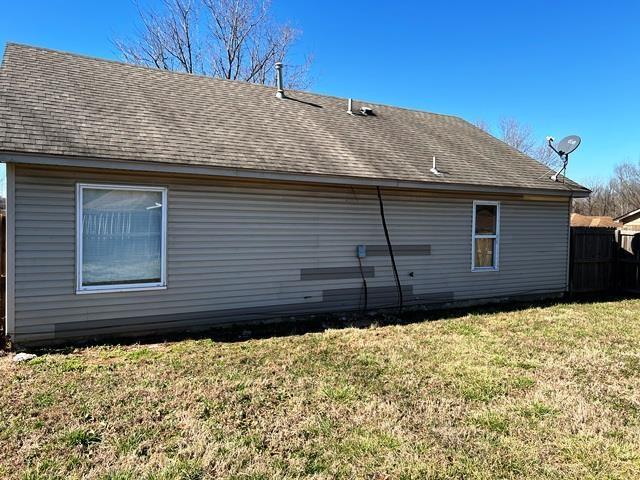 view of home's exterior featuring a shingled roof, a lawn, and fence