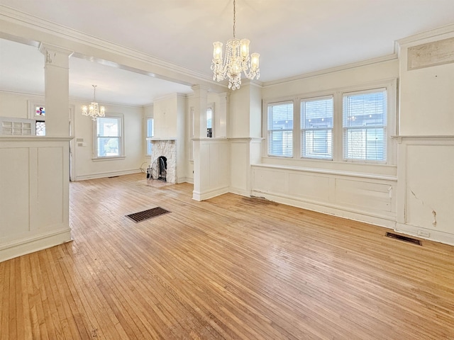 unfurnished dining area with decorative columns, visible vents, ornamental molding, an inviting chandelier, and light wood-style floors