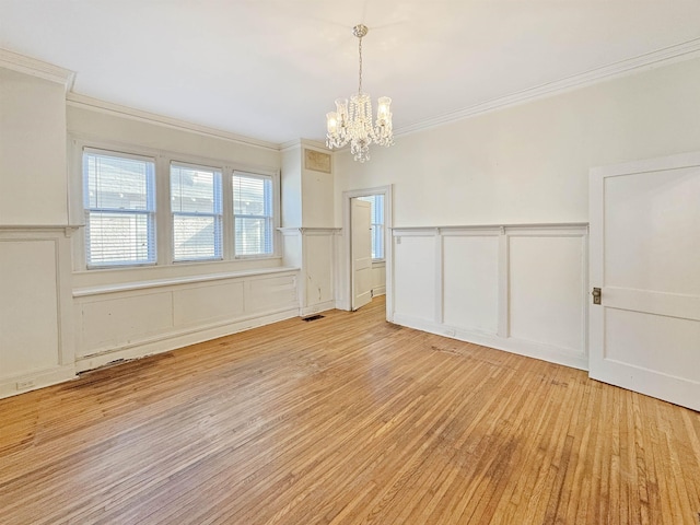 unfurnished room featuring ornamental molding, light wood-style floors, a decorative wall, and an inviting chandelier