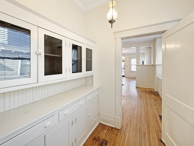 corridor with ornate columns, ornamental molding, light wood-type flooring, and baseboards