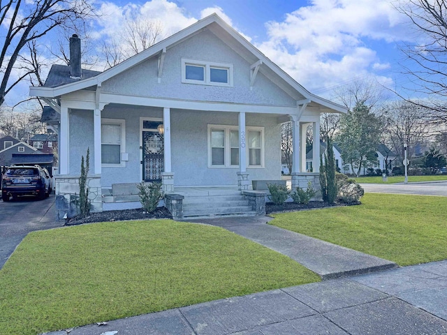 view of front of property featuring driveway, a chimney, covered porch, a front yard, and stucco siding