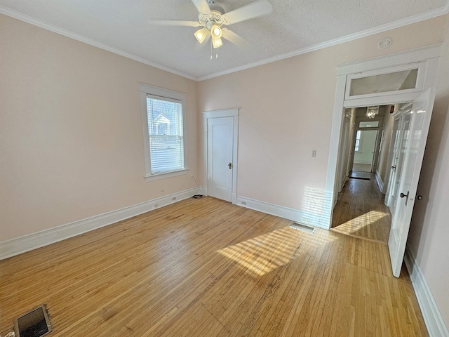 empty room featuring baseboards, light wood-style flooring, visible vents, and crown molding