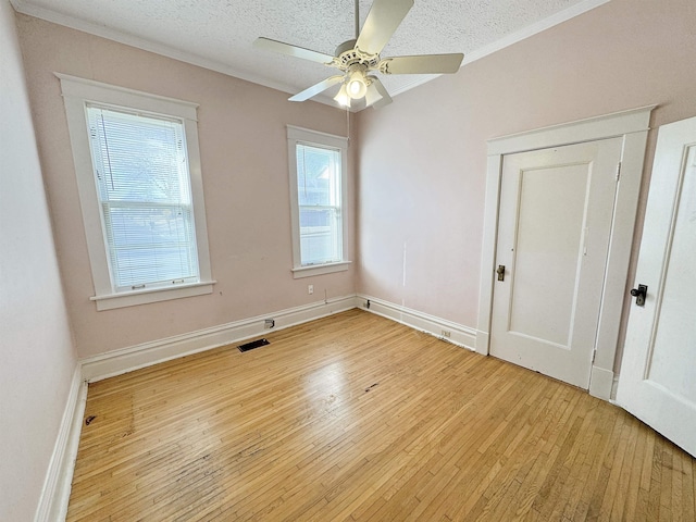 empty room featuring visible vents, a ceiling fan, crown molding, a textured ceiling, and light wood-style floors