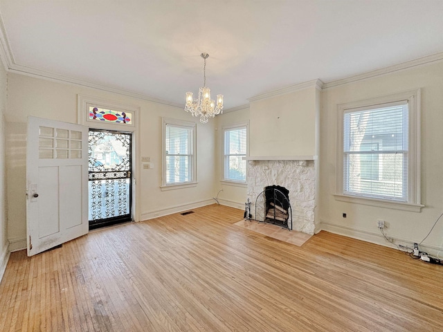 unfurnished living room with light wood-style flooring, a fireplace, visible vents, ornamental molding, and an inviting chandelier