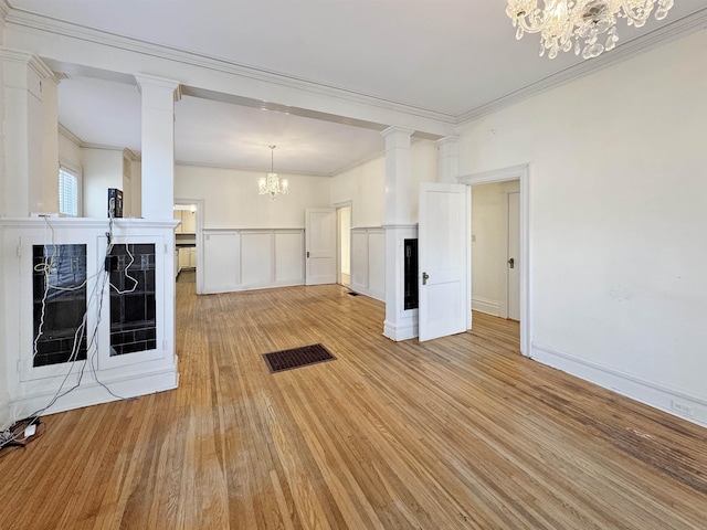 unfurnished living room featuring light wood-type flooring, an inviting chandelier, decorative columns, and ornamental molding