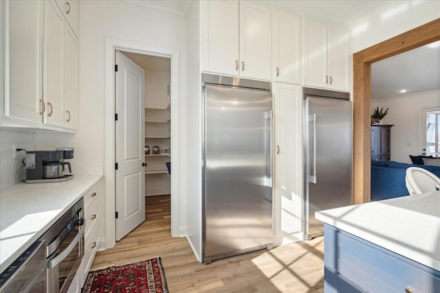 kitchen featuring light wood-type flooring, white cabinetry, appliances with stainless steel finishes, and crown molding