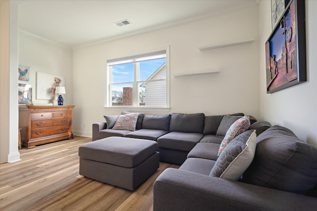 living room featuring baseboards, visible vents, crown molding, and light wood finished floors