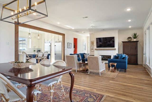 dining area featuring visible vents, ornamental molding, light wood-type flooring, a fireplace, and recessed lighting