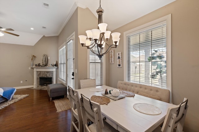 dining space with ceiling fan with notable chandelier, visible vents, vaulted ceiling, a tiled fireplace, and dark wood finished floors