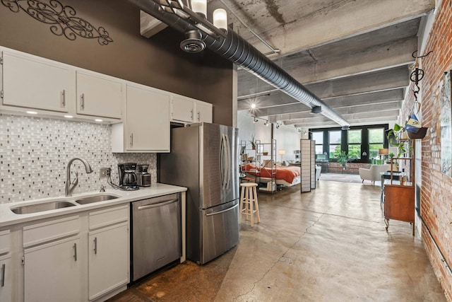 kitchen with brick wall, stainless steel appliances, a sink, white cabinetry, and light countertops