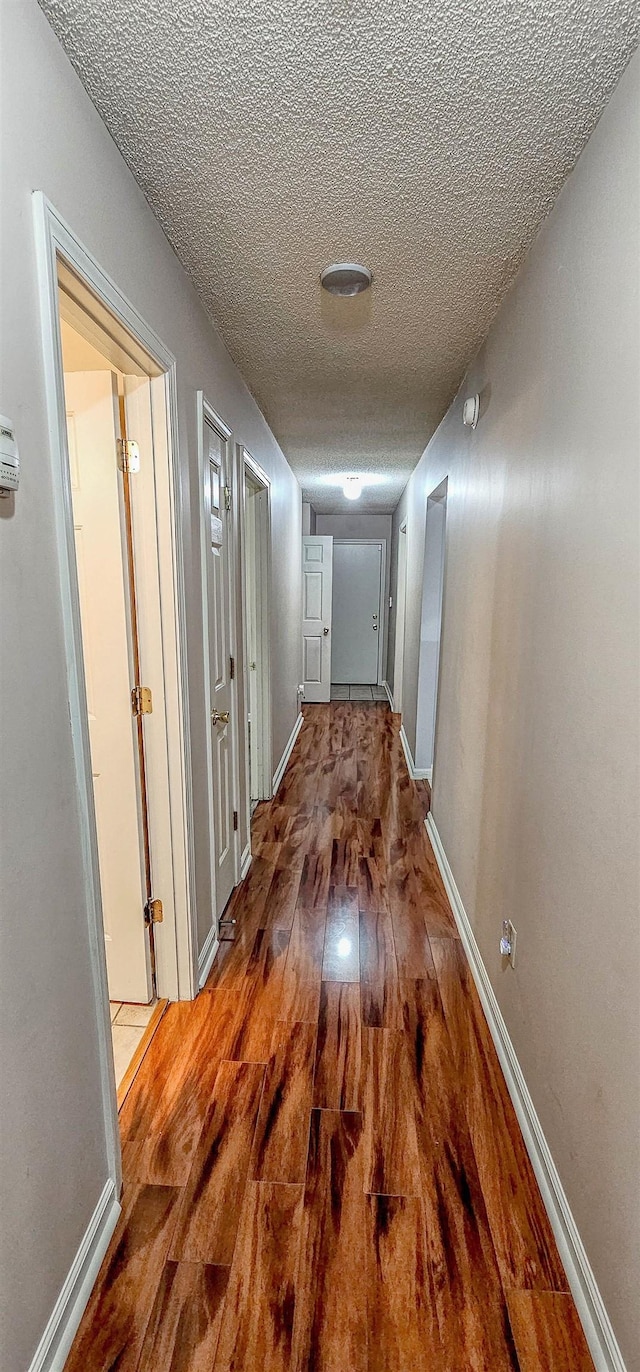 corridor with a textured ceiling, wood finished floors, and baseboards