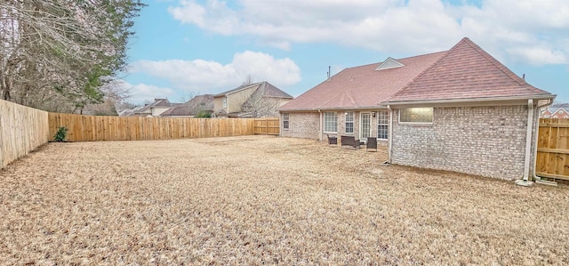 back of house with a fenced backyard, roof with shingles, and brick siding