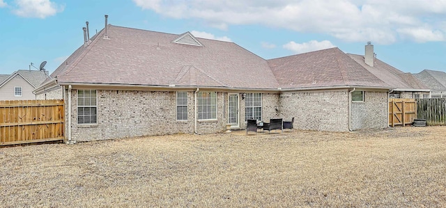 rear view of property with roof with shingles, brick siding, a chimney, and a fenced backyard