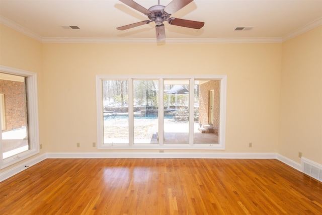 unfurnished room featuring ornamental molding, wood finished floors, visible vents, and baseboards