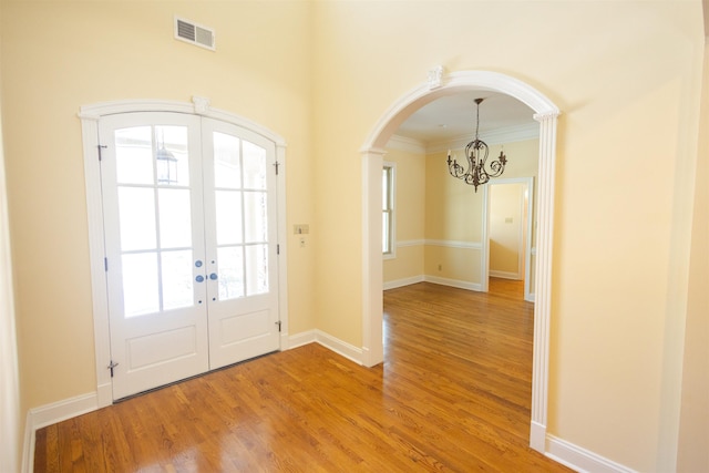 entryway featuring visible vents, arched walkways, wood finished floors, french doors, and a chandelier