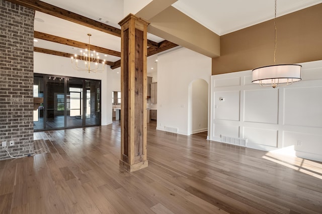 empty room featuring visible vents, wood finished floors, a notable chandelier, a decorative wall, and beam ceiling