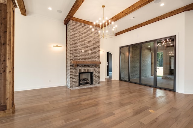 unfurnished living room featuring arched walkways, a fireplace, wood finished floors, baseboards, and beam ceiling