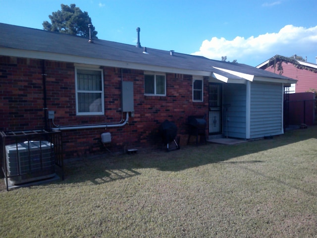 back of house featuring brick siding, a lawn, and central AC unit