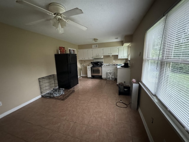 kitchen featuring baseboards, gas range, ceiling fan, a textured ceiling, and white cabinetry