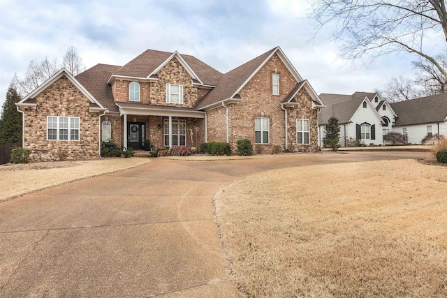 craftsman inspired home featuring stone siding, brick siding, driveway, and roof with shingles