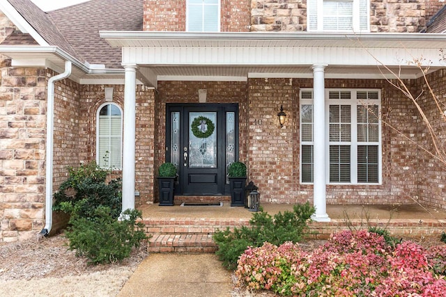 entrance to property with a porch, brick siding, and roof with shingles