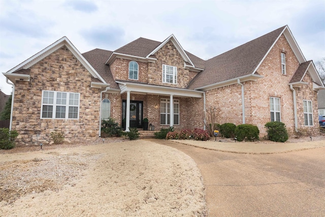 craftsman inspired home featuring stone siding, covered porch, and brick siding