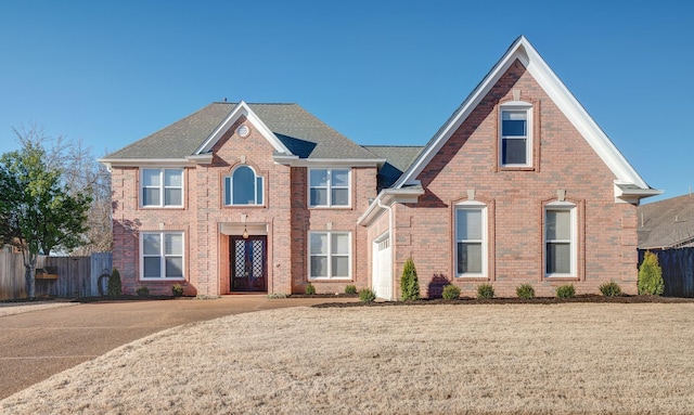 view of front facade with a front yard, brick siding, fence, and roof with shingles