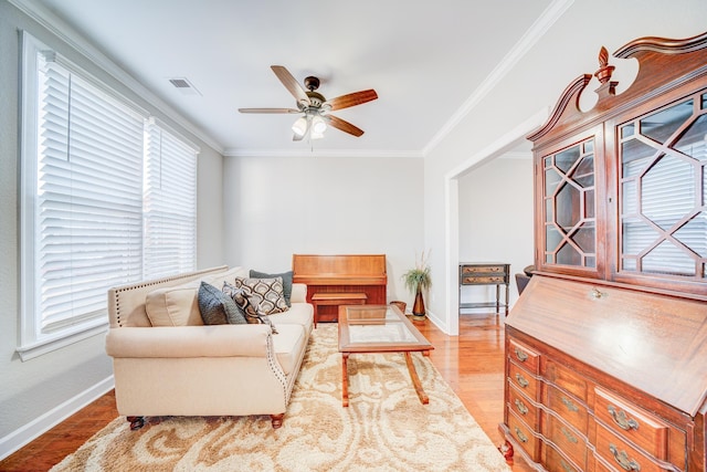 living room with visible vents, a ceiling fan, baseboards, ornamental molding, and light wood-type flooring