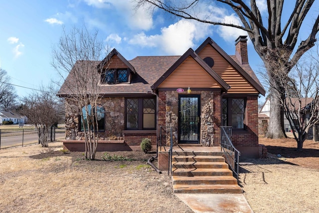 view of front of home featuring brick siding, fence, stone siding, roof with shingles, and a chimney