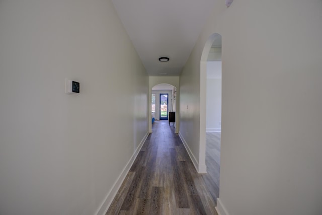 hallway featuring arched walkways, dark wood-style floors, and baseboards