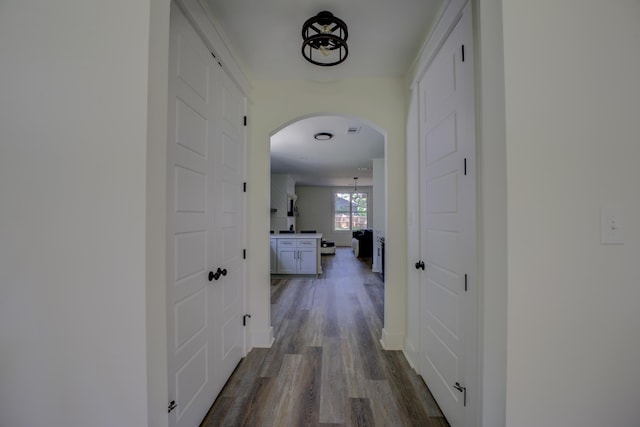 hall featuring baseboards, arched walkways, and dark wood finished floors