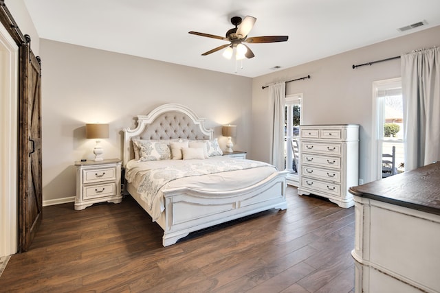 bedroom featuring a barn door, dark wood-type flooring, visible vents, baseboards, and a ceiling fan