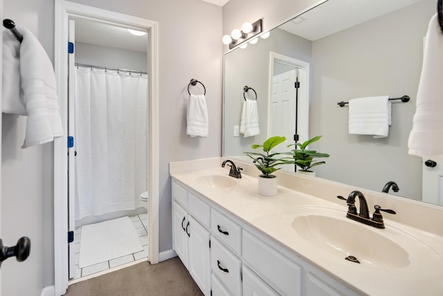 bathroom featuring a textured ceiling, double vanity, a sink, and toilet