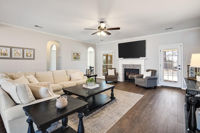 living room featuring ornamental molding, dark wood-style flooring, visible vents, and a fireplace