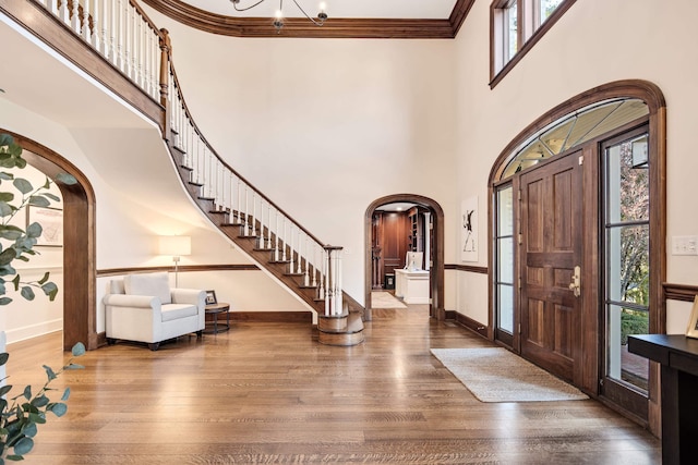 foyer entrance featuring stairway, crown molding, arched walkways, and wood finished floors