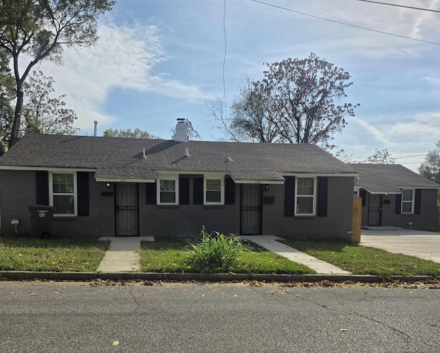 single story home featuring roof with shingles, brick siding, a chimney, and driveway