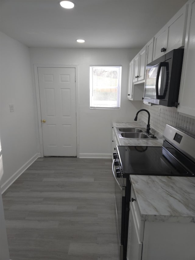 kitchen featuring stainless steel electric stove, white cabinetry, a sink, black microwave, and baseboards