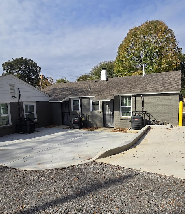 rear view of house featuring central AC, brick siding, roof with shingles, and concrete driveway