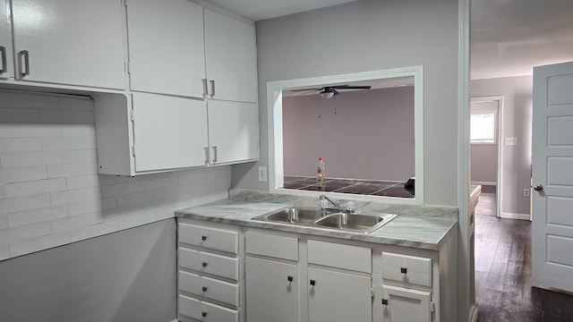 kitchen featuring tasteful backsplash, white cabinets, dark wood-type flooring, light countertops, and a sink