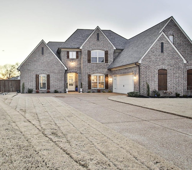 french country style house featuring a shingled roof, brick siding, fence, and driveway